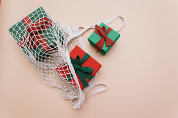 Gifts with ribbons are in a white eco-friendly string bag on a beige background. Top view. Copy space