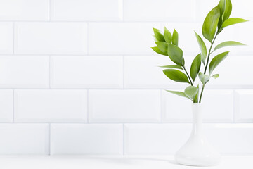 Sunny summer bathroom interior with green bouquet in vase in sunlight, white tiled wall, wood shelf, copy space. Spring interior background for presentation cosmetic products, advertising, design.
