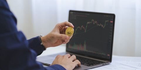 Trade or Investment on Bitcoin Crypto concept. Businessman hand hold gold Bitcoin Cryptocurrency with computer laptop with price graph chart on white desk to analyze for trading and investing. Banner. - 650558630