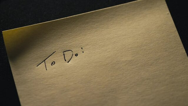 close up of a person starting a To Do list on a white post it note with a pen