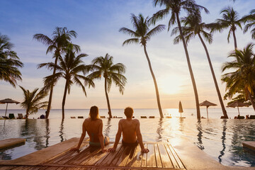 couple on the beach at sunset, honeymoon travel, man and woman sitting near swimming pool in hotel...