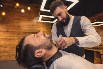 Bearded man getting beard haircut by hairdresser at barbershop.