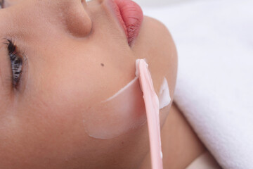 Closeup shot of using a cosmetic spatula to spread RF cream to a patients jawline prior to a Radiofrequency skin tightening treatment. At a facial care, dermatologist or aesthetic clinic.