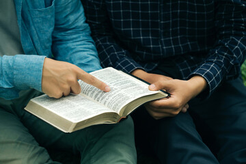 Two men read and studied the bible at the park and prayed together. sharing the gospel with a friend. Holy Bible study reading together on Sunday.Studying the Word Of God With Friends. Education.