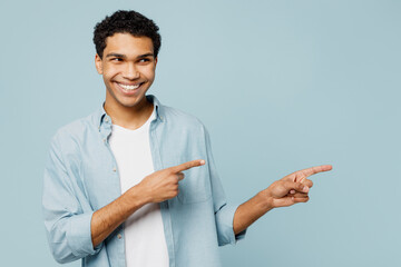Young man of African American ethnicity he wear shirt casual clothes point index finger aside indicate on workspace area copy space mock up isolated on plain pastel light blue cyan background studio.
