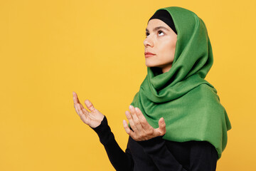 Young arabian asian muslim woman wears green hijab abaya black clothes spread hands praying beg about something isolated on plain yellow background People uae middle eastern islam religious concept