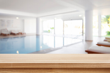 Brown wooden tabletop and blurred summer resort indoor swimming pool - obrazy, fototapety, plakaty