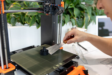 Asian designer engineer using 3D printer in laboratory and studying product prototype.