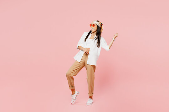 Full body young musician singer latin woman she wear white shirt casual clothes sunglasses pretend playing guitar with hand gesture isolated on plain pastel pink background studio. Lifestyle concept.