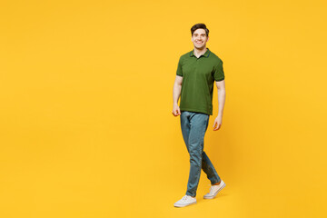 Fototapeta premium Full body side view young caucasian smiling happy man he wears green t-shirt casual clothes walking going strolling look camera isolated on plain yellow background studio portrait. Lifestyle concept.