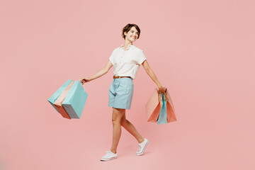 Full body side view fun young woman wear casual clothes hold shopping paper package bags walk go look aside on area isolated on plain pink color background studio. Black Friday sale buy day concept.