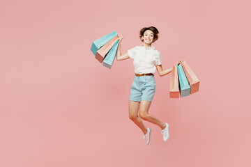 Full body overjoyed excited young woman wears casual clothes hold shopping paper package bags jump...