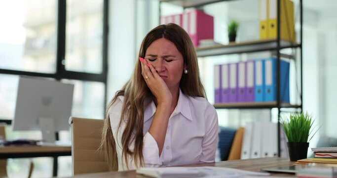 Woman holds cheek and sore tooth at workplace in office. Diagnosis and treatment of pulpitis and acute toothache