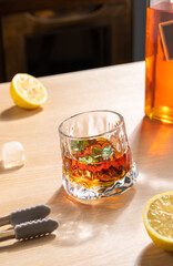 Round glass with whiskey, ice cubes and lemon on the table