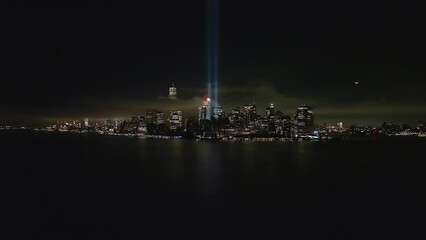 An aerial view of the Freedom Tower in the financial district in New York City at night, with the tribute in light twin beams illuminated. The camera dolly in slowly towards the tall blue lights.