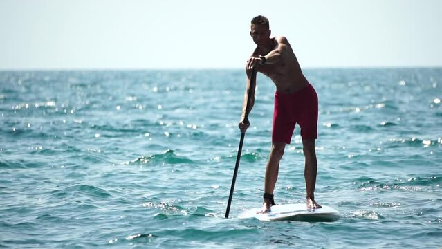 Man Sup Sea. Strong athletic man learns to paddle sup standing on board in open sea ocean on sunny day. Summer holiday vacation and travel concept. Aerial view. Slow motion