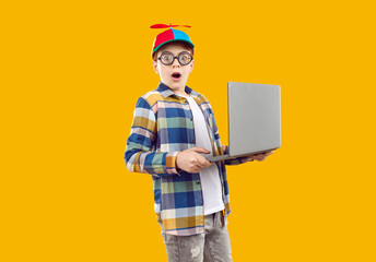 Surprised boy in funny glasses and colored cap with propeller looks directly into the camera,...