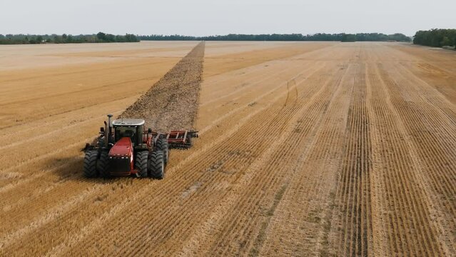 Big red Tractor Pulling Disc Harrow Through Field in Preparation soil for Planting new crops, Agriculture. Aerial view of tractor plowing the field. slow motion video.