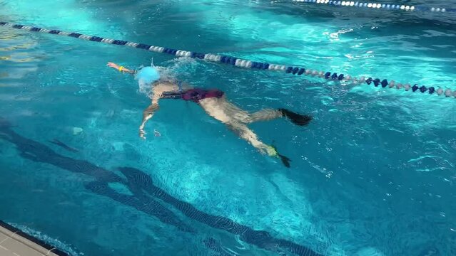 4K A beautiful ten-year-old girl learns to swim. Children practice with fins for swimming in the pool.
