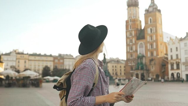 Real view of traveller woman walking on old Market Square in Krakow holding tourist map. Travel and active lifestyle concept. High quality FullHD footage