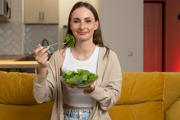 Woman is sitting on a yellow sofa enjoying a nutritious salad for lunch