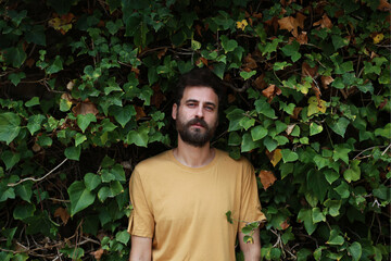 Handsome young man with a beard in a yellow T-shirt on a background of green leaves