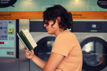 Young woman holding a book in front of a washing machine at the laundromat