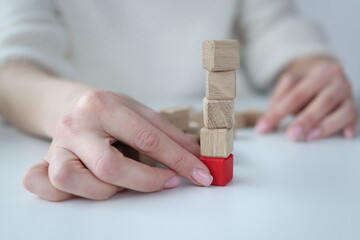 Female hand pulling out red wooden cube from base of tower closeup. Financial pyramid concept