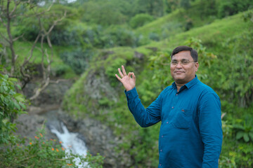 Happy mature Indian asian man with arms crossed standing at nature , Old mustache and brown haired male smiling wearing blue shirt. "selective focus" " shallow depth of field" or " blur".
