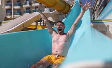 Joyful man slides down slide in water park. Fun in the water park in the summer season concept
