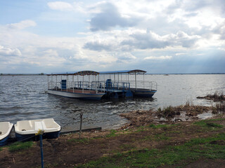 Spring landscape with catamaran and water bikes on the shore of a large lake, against a clear sky....