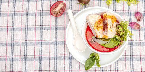 Tomato soup gazpacho ready to eat. Served portion, cutlery. The checkered tablecloth on the table