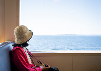 Woman sitting by the window and looking out to the ocean on a ferry ride.