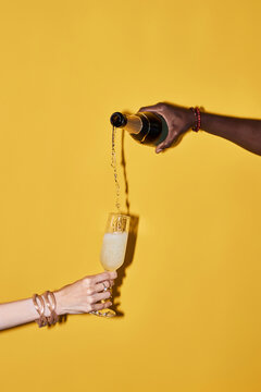 Vertical pop color concept of hands pouring champagne in glass on vibrant yellow background