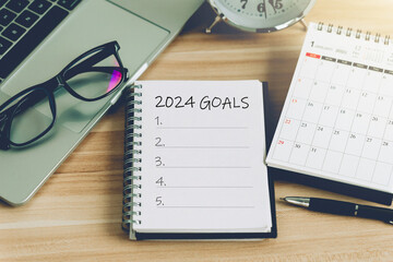 2024 New Year goal, plan, and action concepts. 2024 goals Text on Note Pad with calendar, glasses, and laptop on the table.New Year's resolutions plan.Happy New Year theme, top view, copy space. - obrazy, fototapety, plakaty