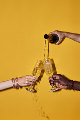 Pop color closeup of hands pouring champagne with splashes against vibrant yellow background