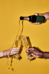 Pop color closeup of people pouring champagne with splashes against vibrant yellow background
