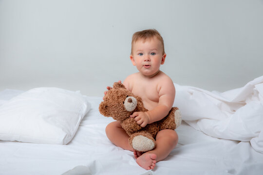 a little baby boy in the bedroom on the bed in a diaper playing with a teddy bear on a white background.