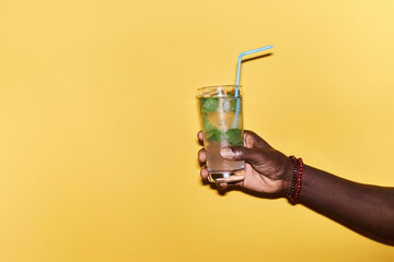Minimal close up of male hand holding refreshing ice cocktail against vibrant yellow background,...