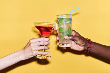 Minimal close up of multiethnic couple clinking cocktails against vibrant yellow background