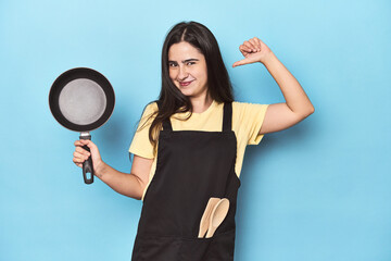 Young woman with pan on blue studio feels proud and self confident, example to follow.