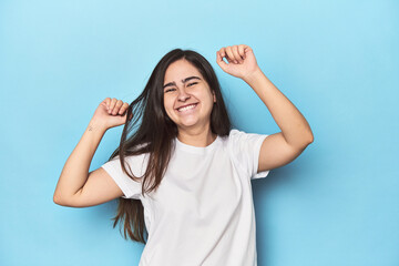 Young Caucasian woman on blue backdrop celebrating a special day, jumps and raise arms with energy.