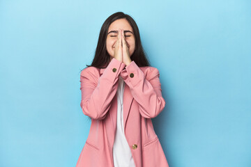 Young Caucasian woman on blue backdrop holding hands in pray near mouth, feels confident.