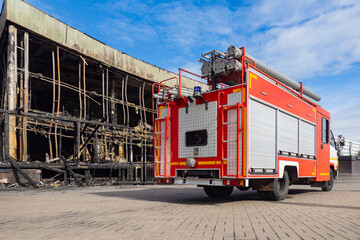Fototapeta premium Rescue vehicle. Burnt out two-story house. Fire service truck. Rescue vehicle rear view. Car for firefighters. Burnt building. Ruins of burnt house. Firefighters transport. Red truck for rescue
