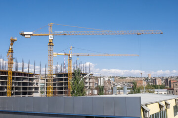 Construction of multi-storey building. Cranes at construction site. Build residential quart in monolithic way. Construction cranes under blue sky. Building industry. Architecture, engineering
