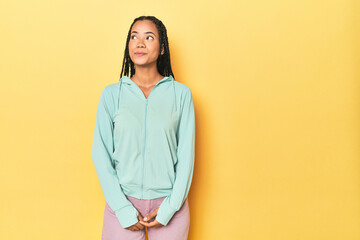 Indonesian sporty woman on yellow backdrop dreaming of achieving goals and purposes