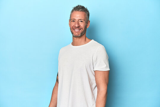 Middle-aged man posing on blue studio backdrop - Powered by Adobe