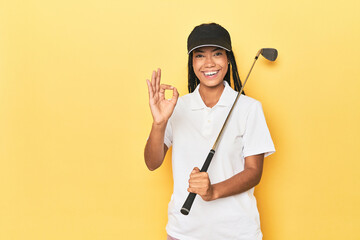 Indonesian female golfer on yellow backdrop cheerful and confident showing ok gesture.