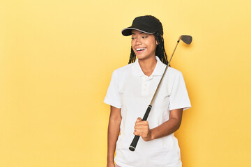 Indonesian female golfer on yellow backdrop looks aside smiling, cheerful and pleasant.