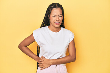Young Indonesian woman on yellow studio backdrop having a liver pain, stomach ache.